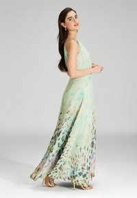 Langes, ärmelloses Kleid in Pastellgrün mit einem Aquarell-Blumenmuster. Der fließende Stoff zeigt eine Mischung aus lila, braunen und schwarzen Akzenten.