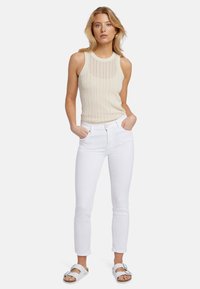 Débardeur en maille beige avec des motifs verticaux, associé à un jean droit blanc et des sandales à boucle argentée. Aucun matériel ou accent visible.