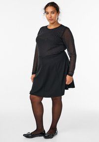 Musta pitkähiha riemukuvioinen paita, yhdistettynä mustaan kellotettuun hameeseen. Mallilla on päällään mustat tasapohjaiset kengät koristeellisilla yksityiskohdilla. Pehmeä tekstuuri.