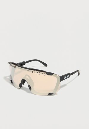 Gafas de sol deportivas envolventes con lentes ventiladas de tono claro y patillas negras con la marca "poc" en los laterales.