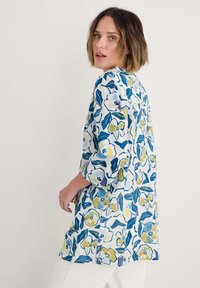 Bloemetuniek van katoen, met een blauw en geel bloemenpatroon, driekwart mouwen en een relaxte pasvorm.