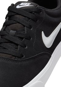 Black suede sneaker with black laces, white accents, and a white logo. Features a textured surface and a contrasting white rubber sole.