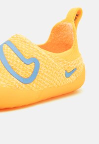 Helle gelbe Slip-On-Schuhe mit einem strukturierten Strickoberteil, einem blauen Akzentlogo und einem weichen Innenfutter. Sie verfügen über eine flexible, gepolsterte Sohle.