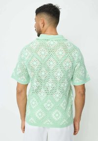 Chemisier en crochet vert menthe avec un design en tricot ouvert et des motifs en diamant et fleuris. Manches courtes et col polo.