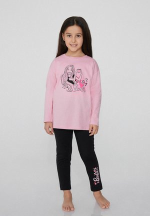 Różowa koszula z długim rękawem z czarnym nadrukiem graficznym przedstawiającym postać i tekst, w połączeniu z czarnymi legginsami z napisem "Barbie" w różowym kolorze.
