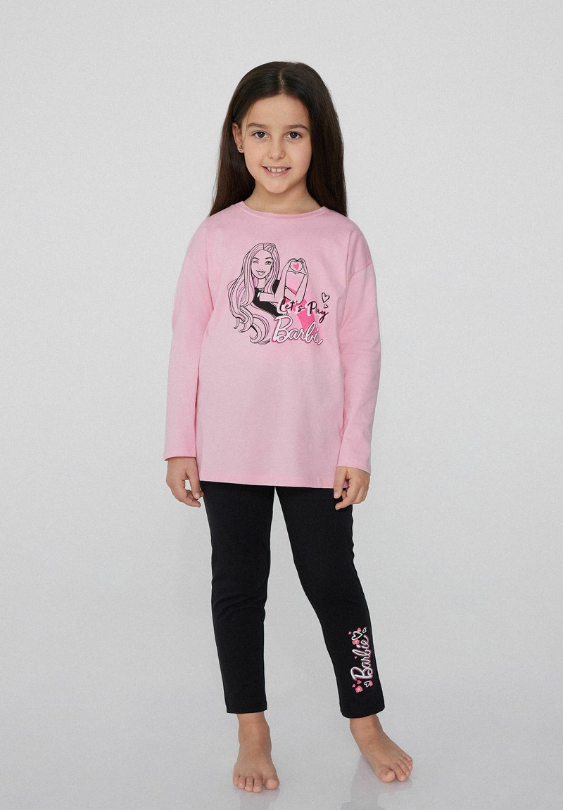 Růžová dlouhá halenka s černým grafickým potiskem znázorňující postavu a text, v kombinaci s černými legínami, na kterých je v růžové napsáno "Barbie".