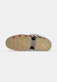 Semelle d'une basket noire et blanche avec une adhérence texturée et un logo circulaire orange au niveau du talon.