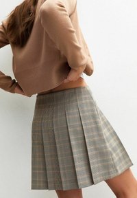 Falda de cuadros con pliegues en tonos beige, marrón y negro, hecha de una tela texturizada. El diseño presenta una cintura alta y pliegues estructurados.