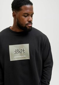 Sort sweatshirt med et rektangulært grafisk tryk med teksten "JACK & JONES" og "DEFINITION OF DENIM SINCE 1990" i hvid og grøn.