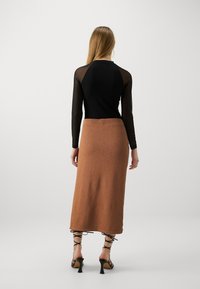Zwarte lange mouwen top met doorschijnende mesh mouwen, gecombineerd met een knielange bruine gebreide rok en open teen zwarte hoge hakken.