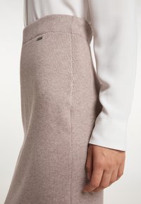 Strick-Midi-Rock in sanftem Blassrosa mit geripptem Muster und elastischem Bund, kombiniert mit einer weißen Bluse mit langen Ärmeln.