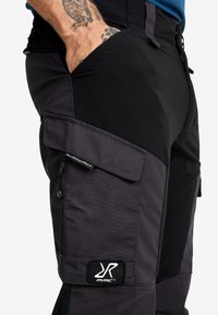 Svart och grå cargobyxor med flera fickor, förstärkta sömmar och en logotyp på sidan. Tillverkade av ett slitstarkt och töjbart tyg.