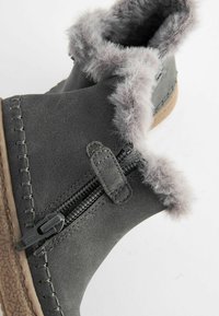 Stivaletto grigio con finitura testurizzata, foderato in morbida pelliccia grigia, con zip laterale e suola marrone leggera con accenti cuciti.