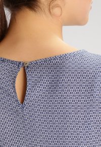 Námořnický top s květinovým vzorem a jemným otvorem ve tvaru klíčové dírky na zádech, který má zapínání na knoflík. Lehce materiál s hladkou texturou.