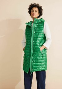 Zelená péřová vesta s kapuc�í, vybavená zipem a patentkami, dvěma postranními kapsami a prošívaným vzorem, nošená přes lehký svetr.