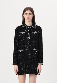 Vestido de tweed preto adornado com lantejoulas, apresentando um decote com gola, detalhes em botões prateados e dois bolsos frontais com adornos semelhantes.