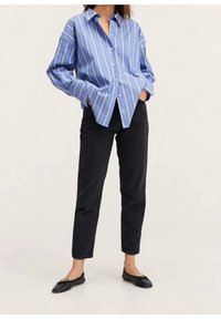 Camisa de botones a rayas azul claro y blanca, de corte relajado, con mangas largas, combinada con jeans negros de corte recto y zapatos planos negros.
