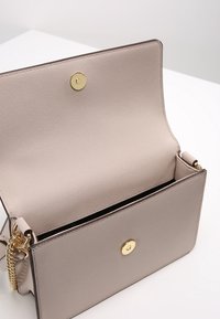 Borsa a tracolla in tessuto beige chiaro con chiusura a scatto dorata, che si apre per rivelare un interno nero. Presenta una tracolla a catena di lato.