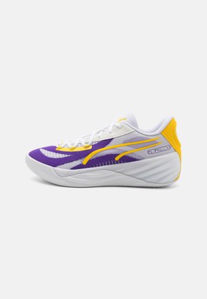 Chaussure avec une tige en maille blanche, accents violets et détails jaunes. Elle dispose d'un bout arrondi et d'une semelle en caoutchouc texturée pour l'adhérence et le soutien.