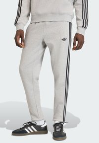 Sive sportske hlače s crnim bočnim prugama, s krojem koji pristaje tijelu i mekom teksturom. Naglašene malim crnim logotipom brenda.