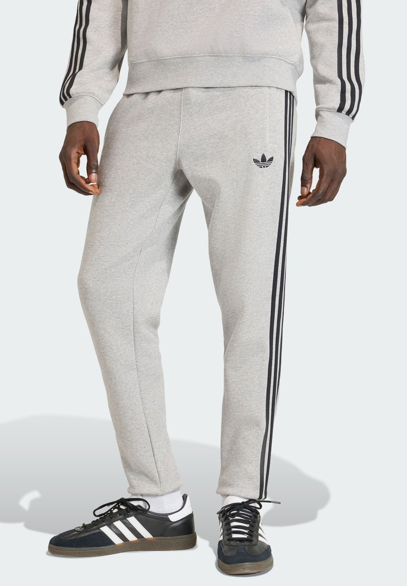 Sive sportske hlače s crnim bočnim prugama, s krojem koji pristaje tijelu i mekom teksturom. Naglašene malim crnim logotipom brenda.