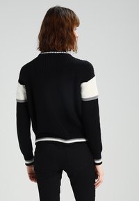 Pull en maille côtelée noire avec des accents blancs sur les manches et une bande blanche à l'ourlet. Présente une coupe décontractée et un col rond.