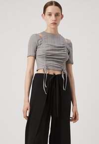 Gray striped cropped top with short sleeves, featuring ruching and ties at the hem, paired with loose black pants. Minimalist design.