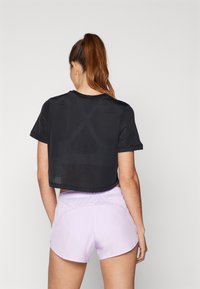 Mustasutta verkkotoppi lyhyillä hihoilla, jota on yhdistetty vaaleanlila shortseihin. T-paidassa on teksturoitu kuvio ja pyöreä helma.