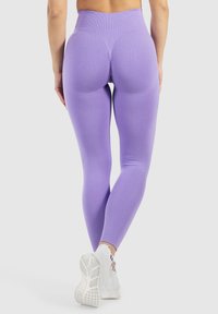 Paarse high-waisted leggings met een gestructureerde afwerking en ruchingdetail aan de achterkant, gedragen met witte sport schoenen.