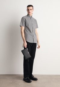 Kortærmet skjorte i sort og hvid tern, sorte bukser, holder en sort lynlåspung, iført sorte sko. Glat stof, slim-fit design.