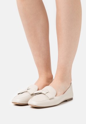 Mocassins en cuir beige clair avec un bout arrondi et un détail nœud à l'avant. Semelle plate, texture lisse et design minimaliste.