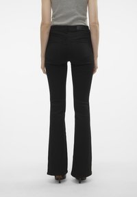 Black flared jeans made of denim, featuring back pockets and a high waist. The hem covers the shoes, creating a streamlined silhouette.