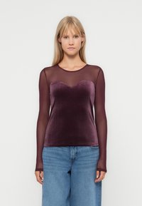 Bordeaux langemouwen top met een doorschijnende mesh overlay en sweetheart halslijn, gecombineerd met blauwe high-waisted jeans. Fluweel textuur detail.