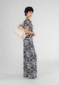 Abito lungo a fiori navy e crema con maniche corte, abbinato a una borsa in pelle beige e a delle scarpe beige con punta.