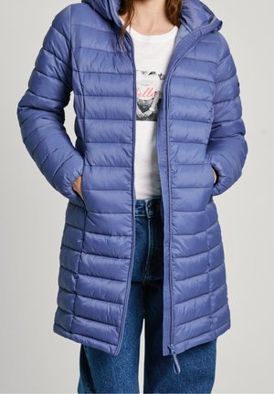 Il cappotto puffer di un leggero viola presenta una texture trapuntata, cappuccio e chiusura con zip. Indossato sopra una maglietta bianca e jeans blu.