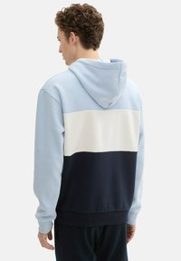 Bluza z kapturem w jasnoniebieskim, białym i granatowym kolorze; wzór w blokach kolorów; miękki materiał; luźny krój; ściągacze przy mankietach i u dołu.