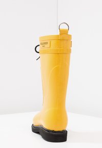 Botte en caoutchouc jaune avec une finition texturée, dotée d'un embout renforcé, d'une boucle en haut pour un enfilage facile, et d'une semelle en caoutchouc noire.