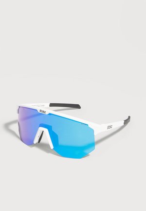 Lunettes de sport à monture blanche avec de grandes verres dégradés bleus et des embouts de branches noirs, exposées sur une surface gris clair.