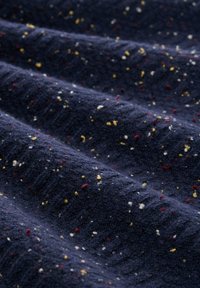 Marineblaue, strukturierte Stoff mit bunten Punkten in Rot, Gelb und Weiß. Weiches, gewebtes Muster mit leichtem Glanz und erhabenem Oberflächengefühl.