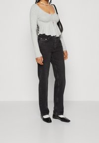 Top gris de manga larga con un dobladillo acampanado, que presenta un cierre frontal con lazo. Combinado con unos jeans negros de pierna recta y unas flats negras de punta.