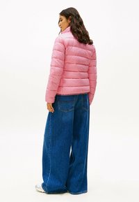 Lyserød pufferjakke med høj krave og horisontal syning, parret med brede blå denimjeans. Glat tekstur og afslappet design.