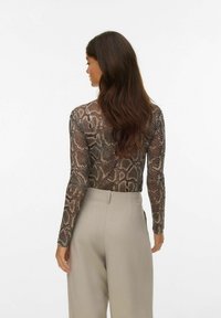 Langarm rompertje van gaasstof met een slangenprint in bruin en beige, gecombineerd met lichtbeige high-waisted broek.