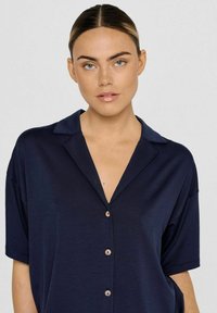 Marineblaue Kurzarmbluse mit durchgehender Knopfleiste, Kragen und glatter Textur. Verfügt über Holzknöpfe zum Schließen.