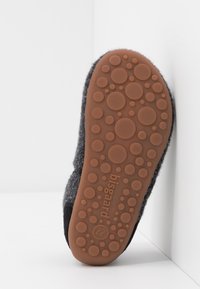 Grijze wollen slof met een bruine rubberen zool, voorzien van ronde uitsteeksels voor grip. De onderkant bevat de merknaam en maat.