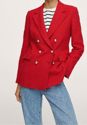 Woman wearing a red double-breasted textured blazer with gold buttons, a black and white striped top, and light blue jeans.