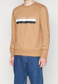 Felpa marrone a maniche lunghe con strisce orizzontali nere, bianche e beige sul petto, realizzata in cotone, con collare e polsini a coste.