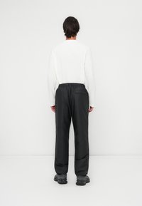 Črne, ohlapne hlače z elastičnim pasom, prikazane s hrbtne strani. Tkanina se zdi lahka in gladka z detajlom žepa.