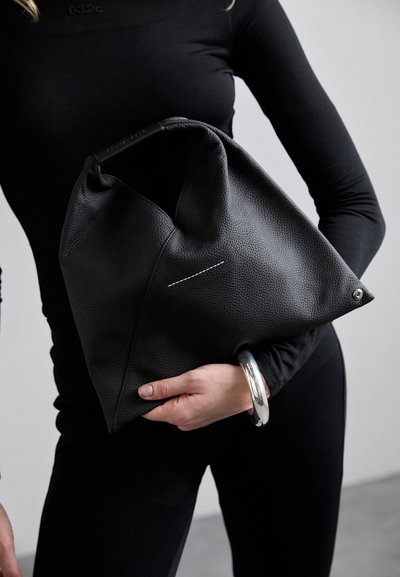 Black leather hobo bag with textured surface, folded design, white stitching detail, and a metallic ring handle.
