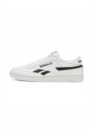 Zapatilla blanca Reebok de corte bajo con rayas laterales negras, logo de Reebok y bandera del Reino Unido en el lateral, cierre de cordones y suela texturizada.