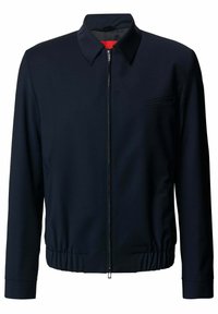 Giacca zip-up blu navy con colletto a punta, vita elastica e tasca sul petto. Tessuto liscio con design minimalista e zip nascosta.